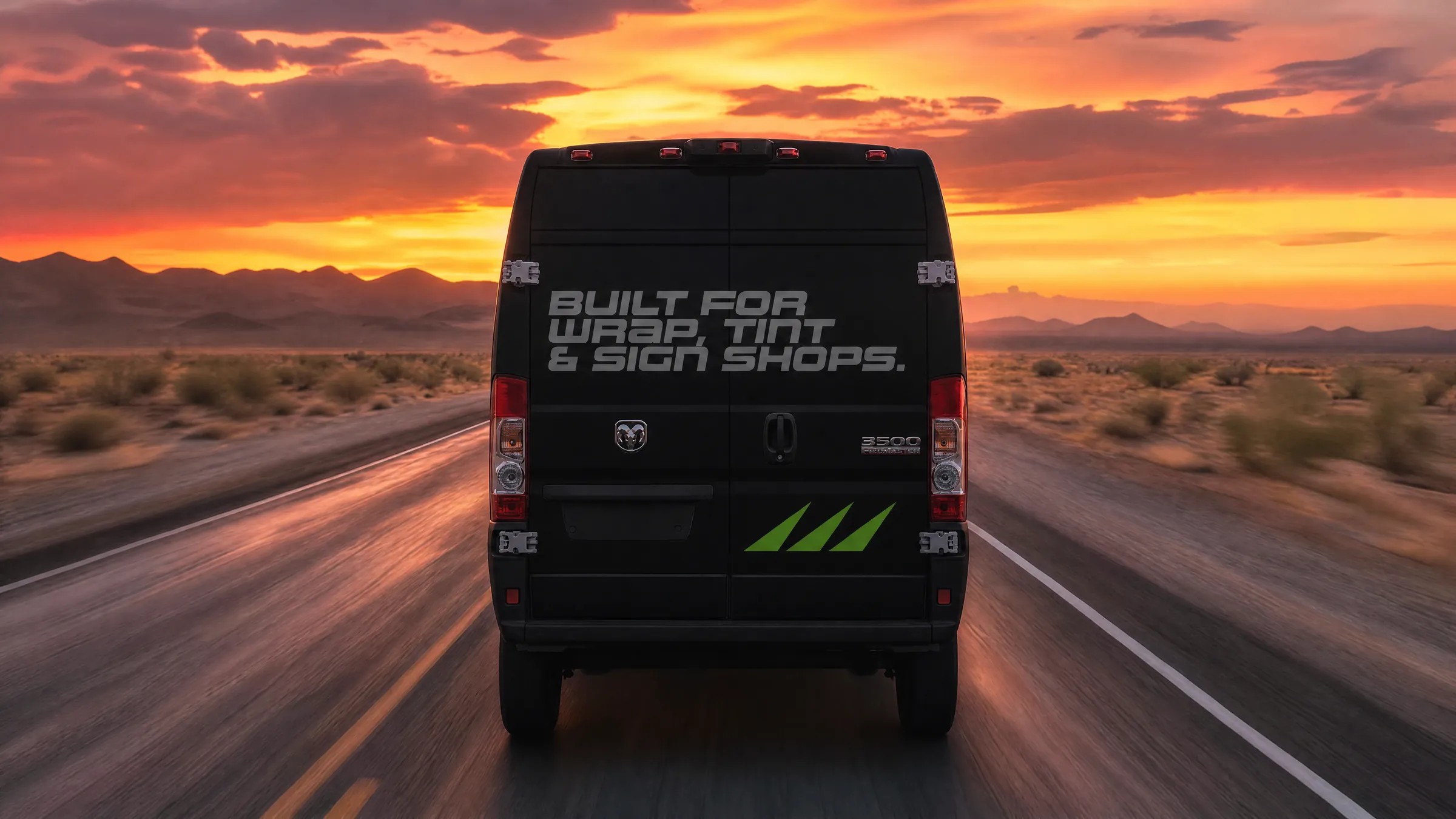 A matte black van reading BUILT FOR WRAP, TINT & SIGN SHOPS driving into a desert sunset
