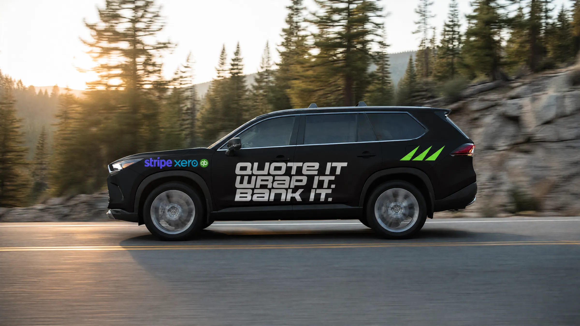 A matte black SUV reading QUOTE IT WRAP IT BANK IT on a mountain road